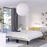 Modern bedroom with RENFJÄLLET bed, white pendant lamp, yellow pillows, bedside table, striped rug, black-white curtains, green view, cosy minimalist.