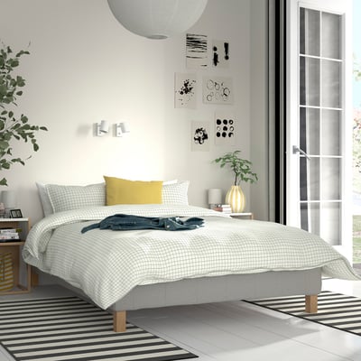 Modern bedroom with RENFJÄLLET bed, grey chequered linens, yellow pillow, wall art, and striped rug.