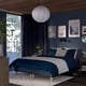 Blue bed, white pillows, wooden nightstands, large window with blue curtains, hanging lamp, wall art, plant.