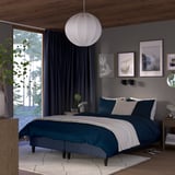 Modern bedroom with large wooden bed, blue/white bedding, hanging light. Decor: art, plant, large windows with tree views.