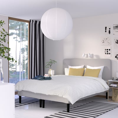 Minimalist bedroom with large bed, big windows, round pendant light, yellow pillows, bedside plants, wall decor, black & white rug.