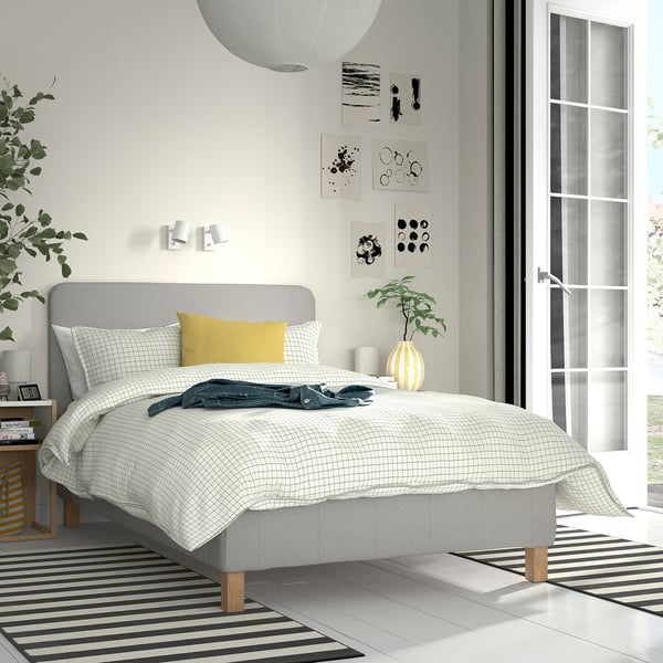 Bedroom with RENFJÄLLET bed, striped rug, books, art, plant.