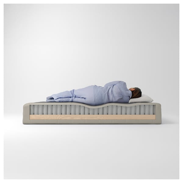 Person sleeping on a mattress with visible coil springs. Light blue walls in the background.