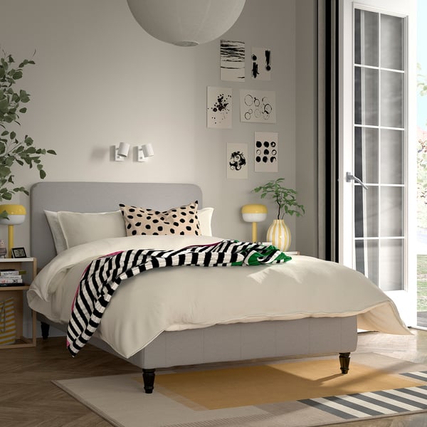 Bedroom with RENFJÄLLET bed, white headboard, black legs, creamy mattress, black/white decor, yellow lamps, abstract art, large off-white light.