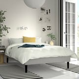 Minimalist bedroom with white RENFJÄLLET bed, yellow pillow, large window, abstract art, and striped rugs.