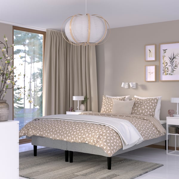 A modern bedroom with a RENFJÄLLET gray and beige bed as the centerpiece, featuring a unique pendant light, beige curtains, and patterned bedding.