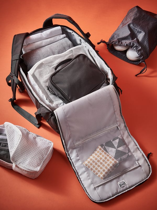 White RENSARE bag on red background, showing organized mesh compartments with clothes and accessories.
