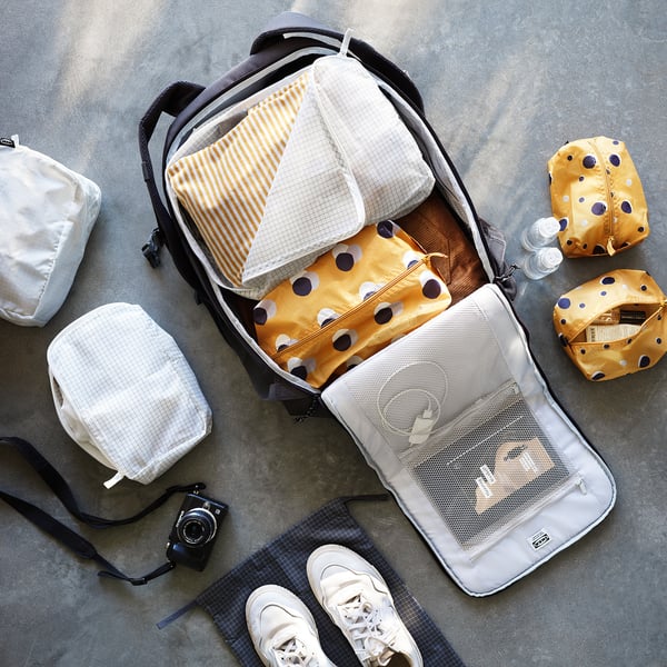 Open backpack with yellow polka dot bags and rolled clothes.