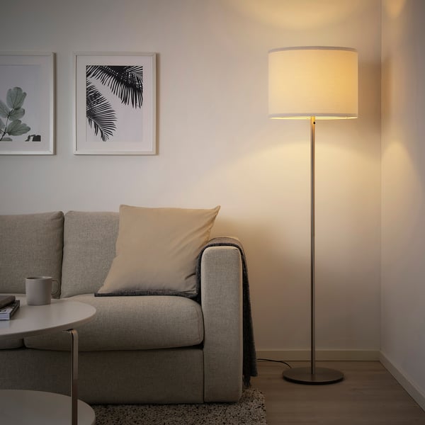 Modern living room with a grey RINGSTA floor lamp, white shade, beside a large couch. The lamp provides soft, diffused light.