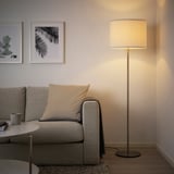 Modern living room with a grey RINGSTA floor lamp, white shade, beside a large couch. The lamp provides soft, diffused light.