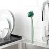 Green kitchen sink brush with suction base, sturdy bristles, scraper edge.