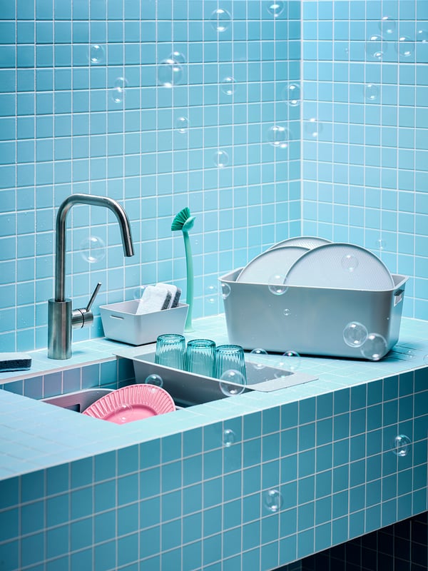 Blue sink with silver faucet, green cleaning tools, pink/blue dishes, blue tiled wall.