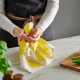 Person wraps lemon-shaped dish towel, likely drying hands or dishes, with kitchen items and plants nearby.