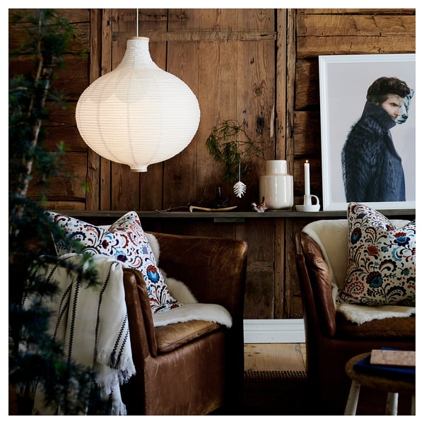 Cozy living space with two leather chairs, colorful pillows, and a hanging white lamp. Wooden walls, bear artwork, and potted plant.