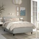 Modern grey bed with upholstered headboard, art on wall, and bedside table with decor. Light enters through french doors.