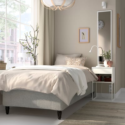 Minimalist bedroom with RISHÖJDEN bed, beige linens, tall bedside table, mirror, and chandelier.