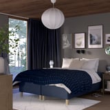 Blue RISHÖJDEN bed with wooden frame, soft pendant light, geometric bedspread, artworks, curtains, window greenery, plant.