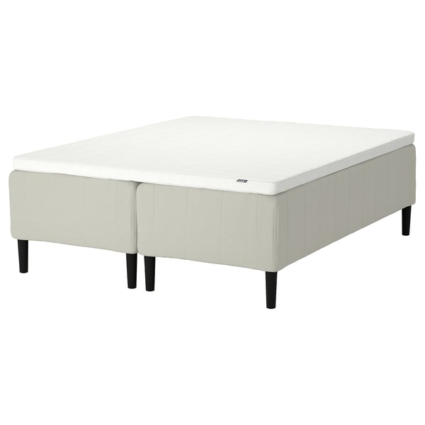 An assembled RISHÖJDEN bed with white mattress and light beige base, featuring reinforced edges and a 7-zone pocket spring system for comfort.