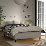 Modern bedroom with RISHÖJDEN bed, large window, yellow lamp, green plant.