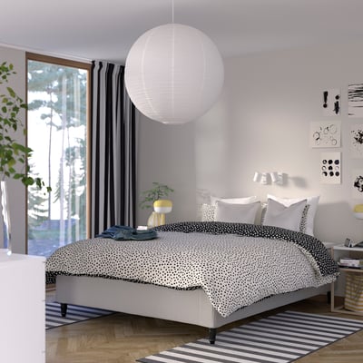 Modern bedroom with RISHÖJDEN bed. White bedding, black polka dots. Large hanging light, large windows. Bed is large, central, with wooden floors.