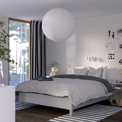 Modern bedroom: polka dot bed, striped rug, pendant lamp, side table with plant, art, basket, forest view.