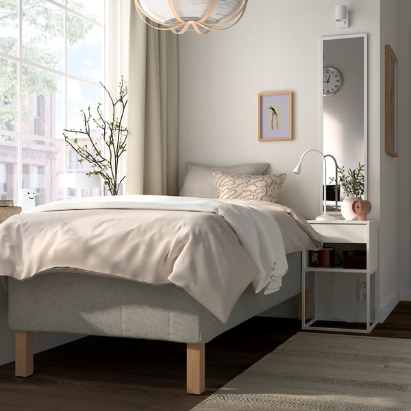 A modern bedroom with a beige bed and white nightstand, featuring a soft light ambiance and minimalist decor.