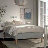 Modern minimalist bedroom with RISHÖJDEN bed, grey linens, wooden nightstands, white lamp, wall art, and large window.