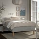 Minimalist bedroom with RISHÖJDEN bed, abstract art, grey bedding, side table with lamp, plant, large window, pendant light.