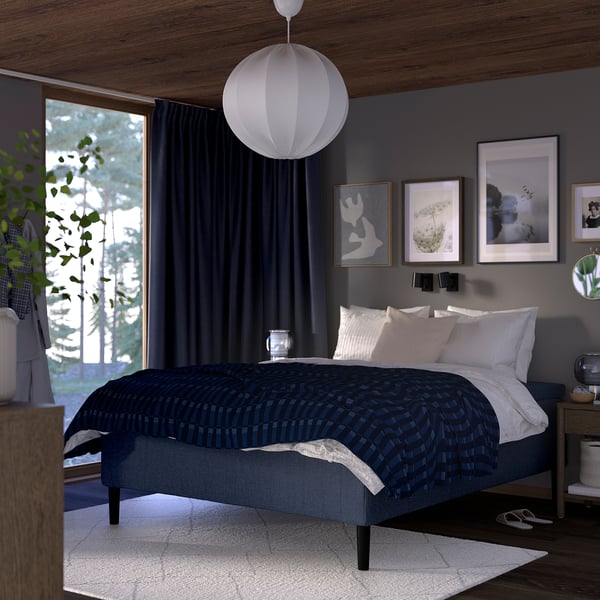 Modern bedroom with dark blue RISHÖJDEN bed; large white rug, hanging lamp, dark walls; wall art, large window with curtains.