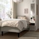 Cosy bed with RISHÖJDEN base, grey mattress, decorative pillows, bedside table with lamp, large window.