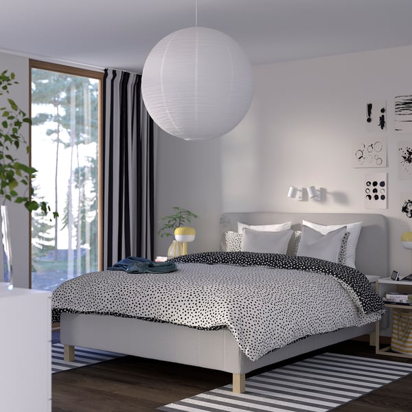A minimalist bedroom with RISHÖJDEN bed, white bedding, large pendant light, gray curtains, plant, and rug. Decorated with wall art.