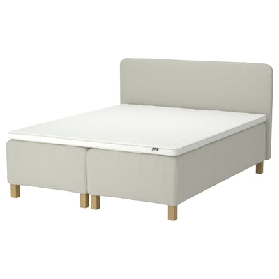 Modern bed with beige upholstered headboard & base, wooden legs, white mattress, 7 comfort zones.