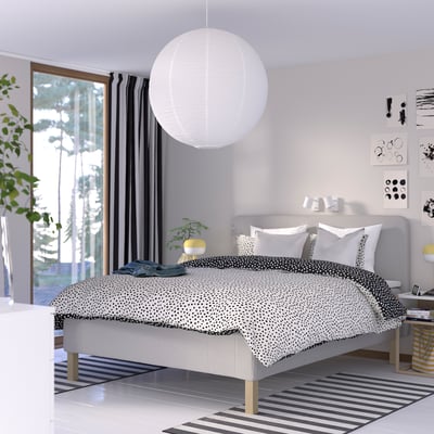 A stylish bedroom with a white RISHÖJDEN bed, polka-dot duvet, large pendant lamp, striped rug, modern wall decor, sliding glass door, and a plant.