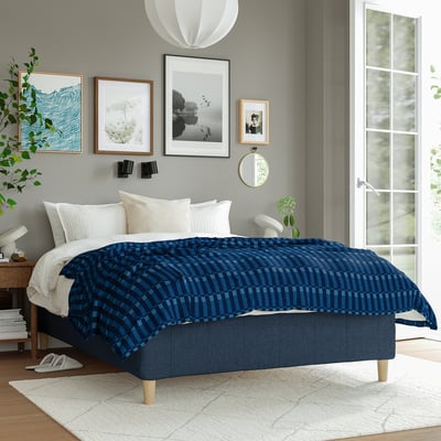 Bedroom with dark blue RISHÖJDEN bed, grid spread, pillows, shoes, and artwork.