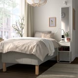 Minimalist bedroom with RISHÖJDEN bed, white, wood, grey linens. Fits neatly under window, beside table holds books.
