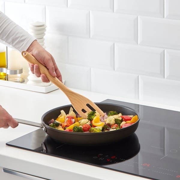 Person stirring colorful veggies in non-stick pan on induction cooktop.