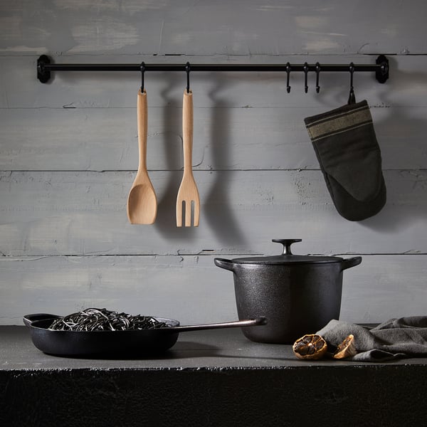 Kitchen utensils hang from bar; counter with noodles, oranges. Aged wall. This version retains the main elements while being concise.