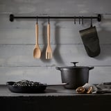 Kitchen utensils hang from bar; counter with noodles, oranges. Aged wall. This version retains the main elements while being concise.