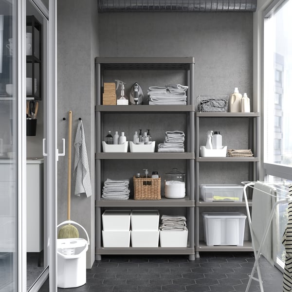 Gray storage shelf with multiple levels holding clothes and supplies against wall, next to mop and bucket.