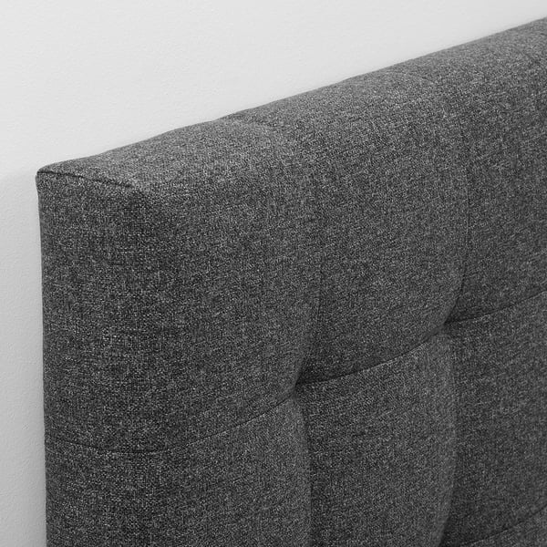 Soft, grey, upholstered headboard with detailed stitching, mounted on a white wall.