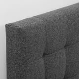 Soft, grey, upholstered headboard with detailed stitching, mounted on a white wall.