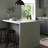 Modern kitchen with SÄLJAN light grey stone-patterned countertop, dark stools, pendant lamp, and plants.