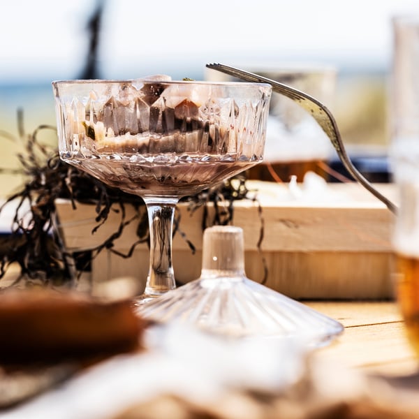 Clear glass bowl with a golden spoon, filled with brown dessert. A transparent glass container with a white lid sits nearby.