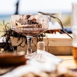 Clear glass bowl with a golden spoon, filled with brown dessert. A transparent glass container with a white lid sits nearby.