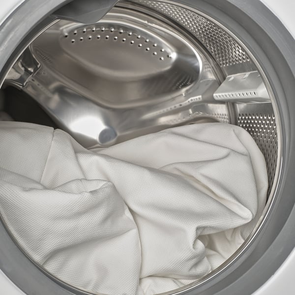 Stainless steel washing machine loaded with laundry, drum with perforated plate, white fabric inside.