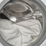 Stainless steel washing machine loaded with laundry, drum with perforated plate, white fabric inside.