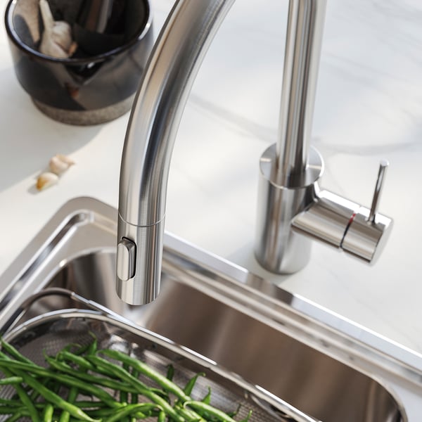 Modern kitchen tap with sleek stainless steel finish and pull-out sprayer. Green vegetables in sink.