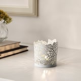 Tealight holder with leaf cutout, candlelit. Nearby, dried flowers and books create cozy decor.