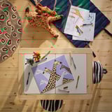 Giraffe-themed play area with stuffed toy, blue blanket, coloring sheet, and zebra cushion.