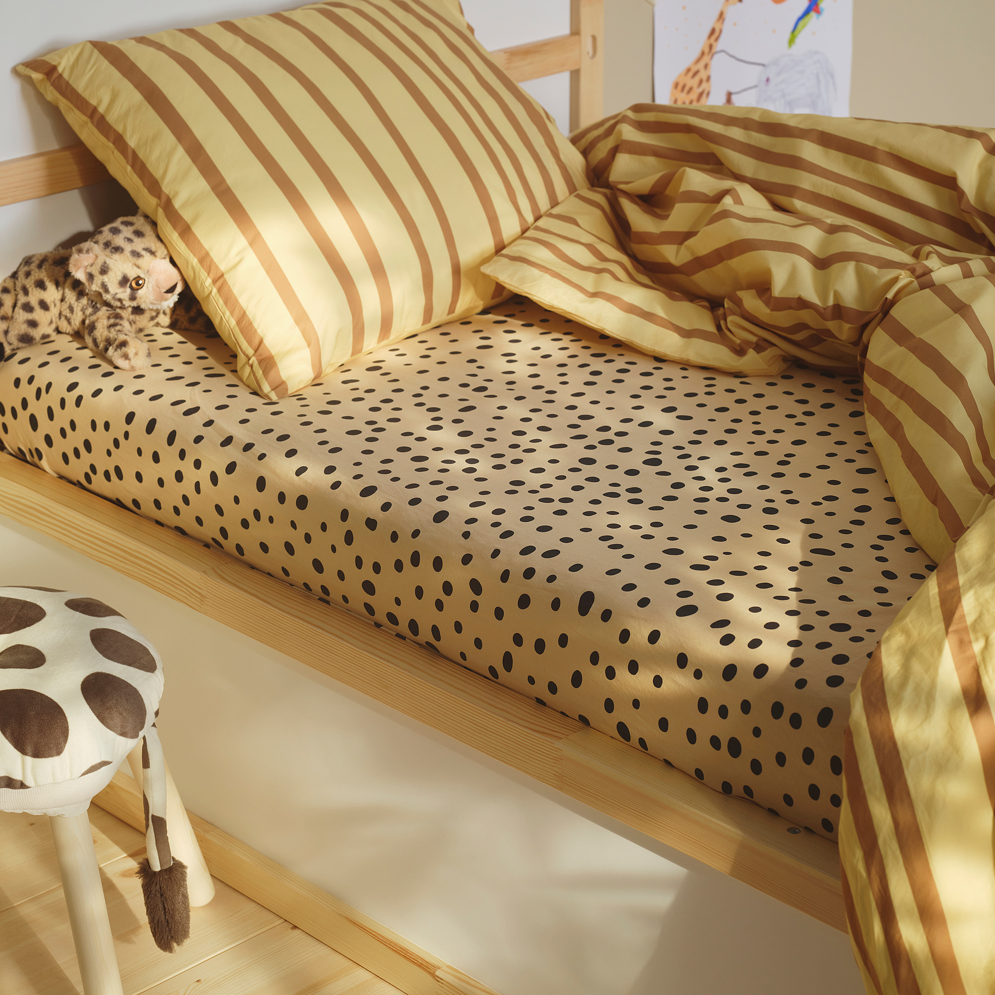 Safari-themed kids bed with SANDLÖPARE fitted sheet in brown spots. Includes striped pillows, a leopard plush, and a giraffe stool nearby.